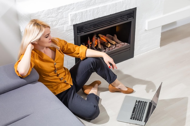 Donna sorridente felice che usa il laptop nel soggiorno di casa, guardando video divertenti, imparando la lingua, videochiamate, madre che lavora online