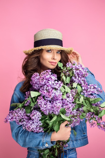 Donna sorridente felice in cappello di paglia che posa con il mazzo dei fiori lilla