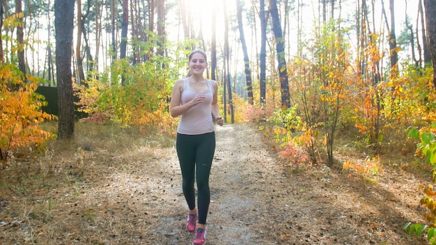 Donna sorridente felice in leggings in esecuzione nella foresta in giornata di sole.