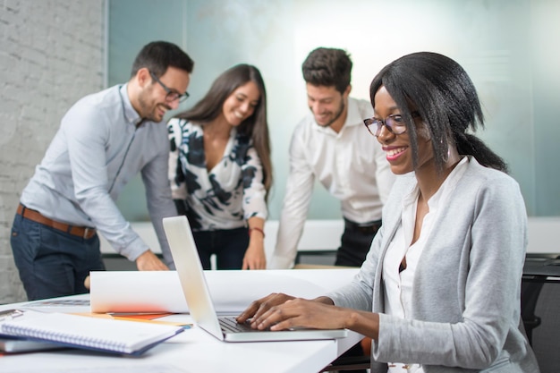 Donna sorridente in abbigliamento da lavoro che lavora sul portatile alla sua scrivania in ufficio