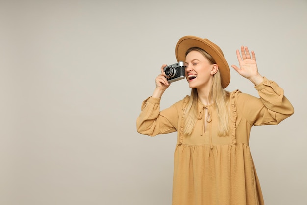 Donna sorridente in cappello che tiene macchina fotografica d'epoca su sfondo grigio spazio per il testo