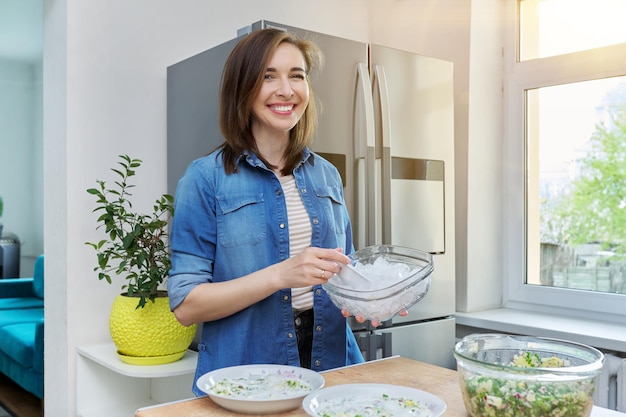 Donna sorridente in cucina vicino al frigorifero con ghiaccio per raffreddare il cibo
