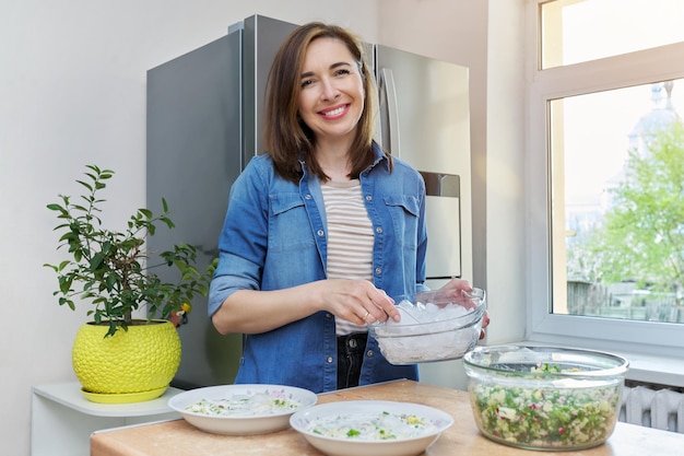 Donna sorridente in cucina vicino al frigorifero con ghiaccio per raffreddare il cibo