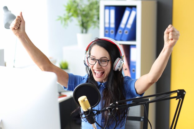 Donna sorridente in cuffia che si rallegra davanti al microfono al lavoro radiofonico della stazione radio