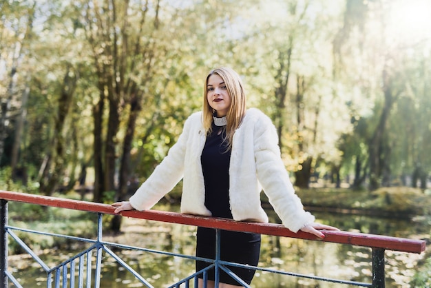 Donna sorridente in giacca di pelliccia in posa nella foresta autunnale. Pelliccia e moda