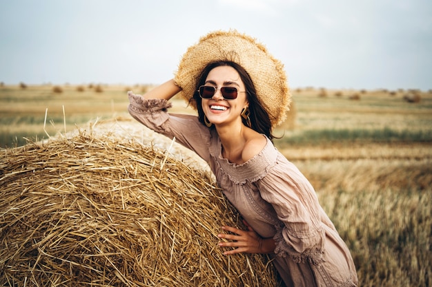 Donna sorridente in occhiali da sole con spalle nude sul campo di grano e balle di fieno