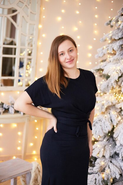 Donna sorridente in piedi vicino all'albero di Natale Felice anno nuovo e buon Natale