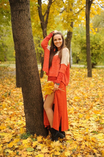 Donna sorridente in posa nel parco autunnale, vestita con un maglione e una gonna arancioni casual