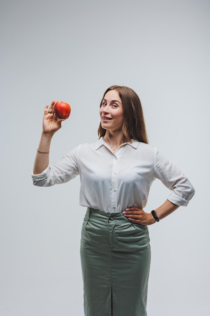 Donna sorridente in possesso di una mela rossa Bella bruna in una camicia bianca Cibo vegetale sano e vitamine Sfondo bianco