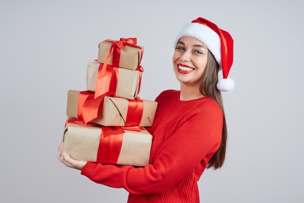 Donna sorridente in santa cappello, maglione rosso, con in mano un mazzo di regali con un nastro rosso. Concetto di vacanza, Natale e Capodanno.