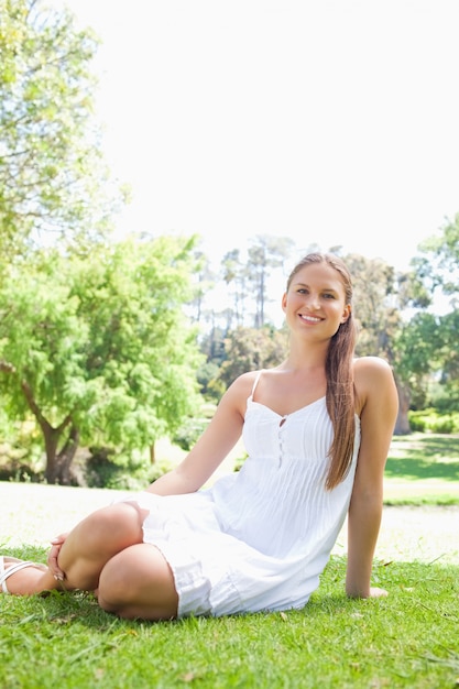 Donna sorridente nel parco che si siede sul prato