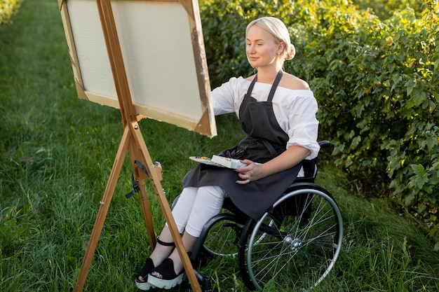 Donna sorridente nella pittura su sedia a rotelle in natura