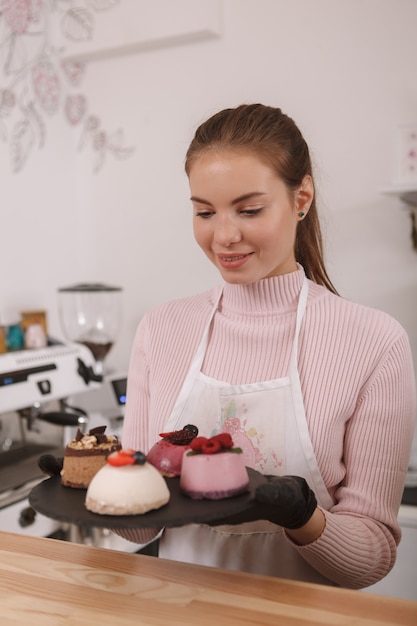 Donna sorridente, portando dolci su un piatto, lavorando nella sua caffetteria