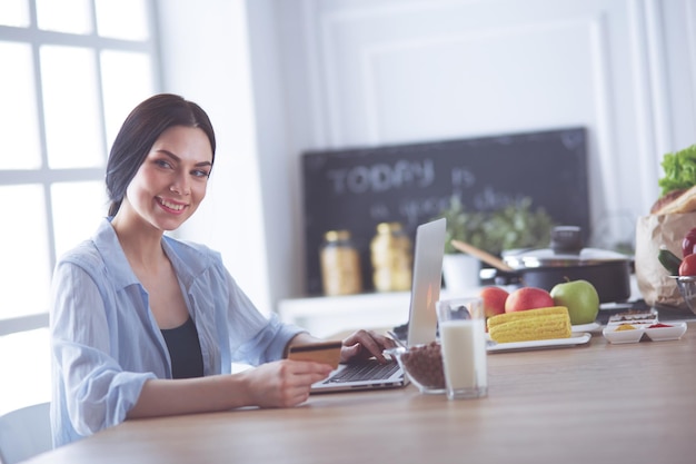 Donna sorridente shopping online utilizzando tablet e carta di credito in cucina