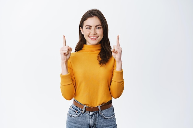 Donna sorridente sicura in maglione giallo che guarda con la faccia sicura di sé su bianco