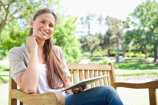 Donna sorridente su una panchina del parco con il suo tablet PC