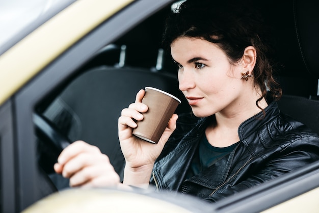 Donna sorseggiando un caffè durante la guida di un&#39;auto.