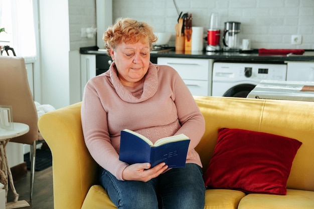 Donna sovrappeso che legge un libro seduta sul divano in soggiorno