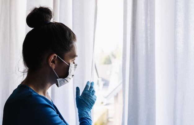 donna spaventosa in quarantena corona che guarda fuori dalla finestra sulla strada