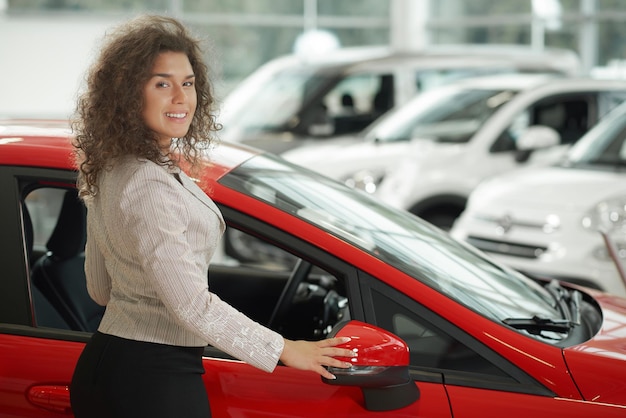 Donna splendida che posa vicino all'automobile rossa nel centro dell'automobile