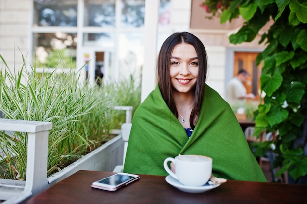 Donna splendida del brunette che si siede sulla tabella in plaid della copertura del caffè con la tazza di caffè.