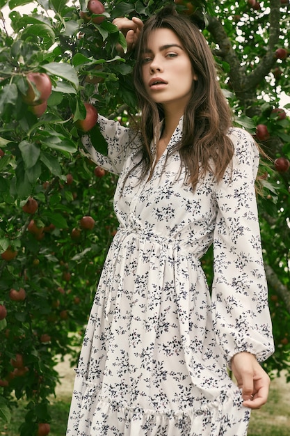 Donna splendida del brunette in vestito classico da modo nel giardino delle mele