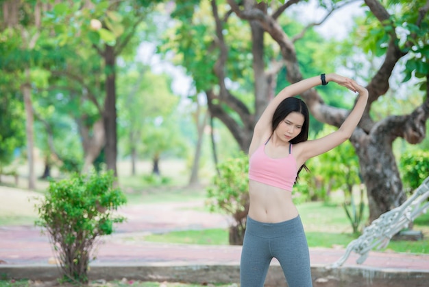 Donna sportiva asiatica che allunga il corpo respirando aria fresca nel parco Concetto di fitness ed esercizio