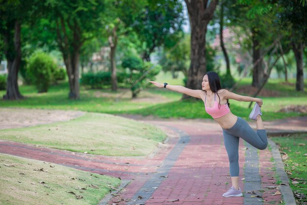 Donna sportiva asiatica che allunga il corpo respirando aria fresca nel parco Concetto di fitness ed esercizio