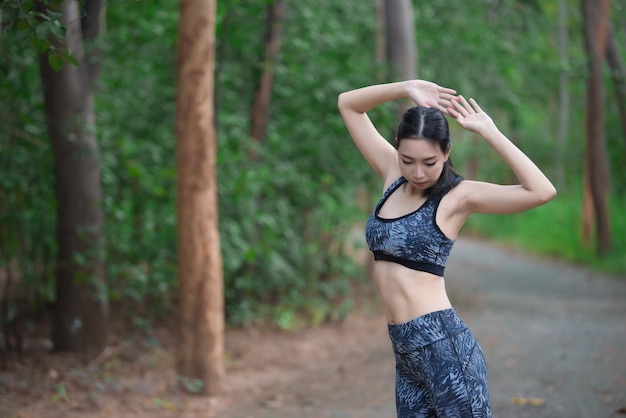 Donna sportiva asiatica che allunga il corpo respirando aria fresca nel parco Persone Thailandia Concetto di fitness ed esercizio Fare jogging nel parco Scaldare il corpo Sedersi per scarpe con lacci
