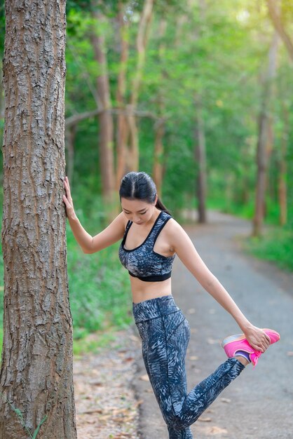 Donna sportiva asiatica che allunga il corpo respirando aria fresca nel parcoThailandia personeFitness e concetto di esercizio Jogging nel parcoRiscaldare il corpo