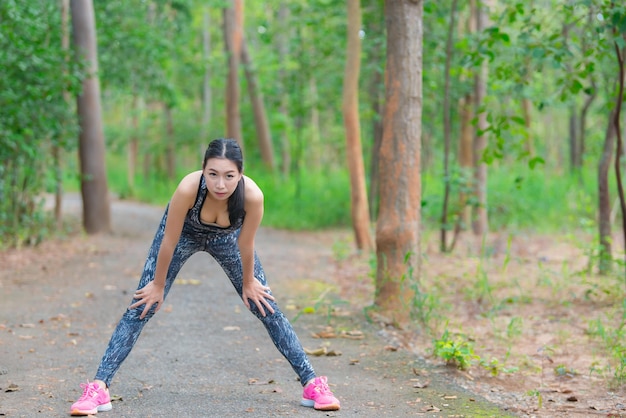 Donna sportiva asiatica che allunga il corpo respirando aria fresca nel parcoThailandia personeFitness e concetto di esercizio Jogging nel parcoRiscaldare il corpo