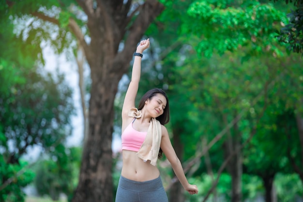 Donna sportiva asiatica che allunga le braccia respirando aria fresca nel concetto di esercizio della gente del parcoThailandia