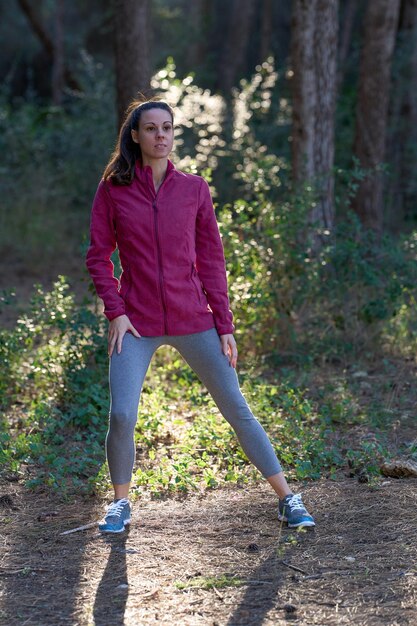 Donna sportiva che allunga le gambe nella foresta in abbigliamento sportivo verticale