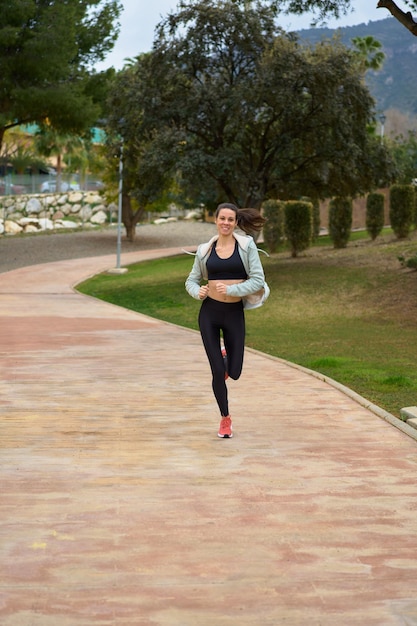 Donna sportiva che corre nella vista frontale del parco sorridente in felpa e leggings