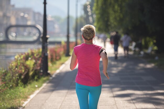 donna sportiva che corre sul marciapiede al mattino presto con la scena dell'alba della città sullo sfondo