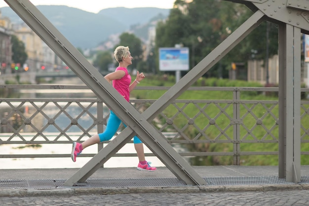 donna sportiva che corre sul marciapiede al mattino presto con la scena dell'alba della città sullo sfondo