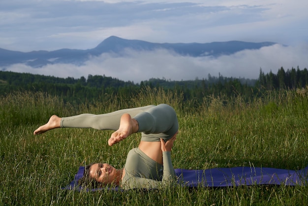 Donna sportiva che fa acro yoga tra le montagne verdi