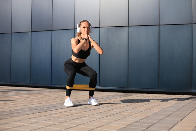 Donna sportiva che fa squat con espansore di gomma fitness all'aperto.