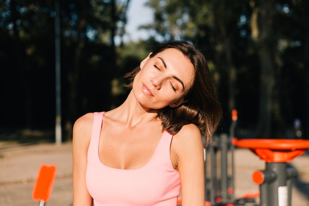 Donna sportiva che indossa abbigliamento sportivo al tramonto al campo sportivo allungando il collo prima dopo l'allenamento