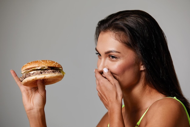 Donna sportiva che mangia cibo malsano su sfondo chiaro Concetto di dieta