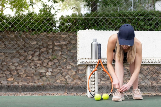 Donna sportiva che si prepara e si prepara per giocare a tennis che lega i lacci delle sue scarpe all'aperto