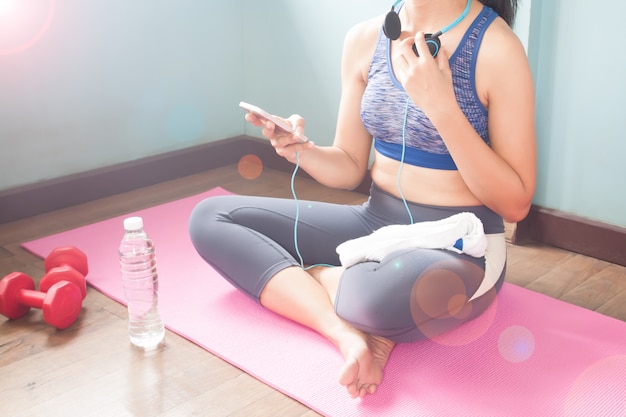 Donna sportiva che si siede sulla stuoia di yoga utilizzando il telefono cellulare