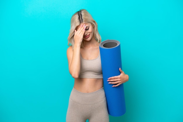 Donna sportiva che va a lezioni di yoga mentre tiene un tappetino isolato su sfondo blu con espressione stanca e malata