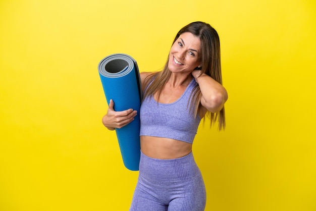 Donna sportiva che va a lezioni di yoga mentre tiene un tappetino isolato su sfondo non giallo ridendo