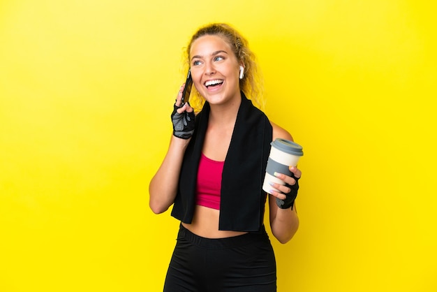 Donna sportiva con asciugamano isolato su sfondo giallo che tiene caffè da portare via e un cellulare