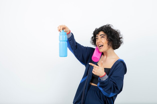 Donna sportiva dai capelli corti riccia che sceglie quale bottiglia d'acqua portare in palestra.