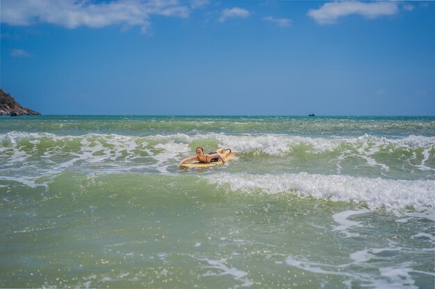 Donna sportiva del surfista dell'onda di giro della bella giovane donna che pratica il surfing sui precedenti delle nuvole del cielo blu e