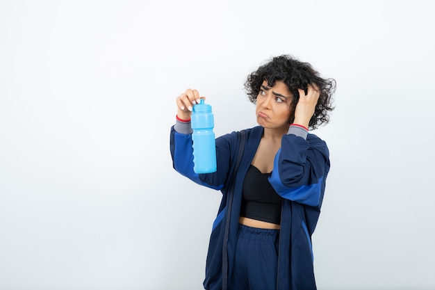 Donna sportiva di bella misura che tiene la bottiglia di acqua blu.