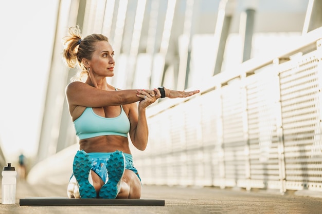 Donna sportiva di mezza età che si riscalda e allunga le braccia su un ponte.