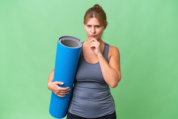 Donna sportiva di mezza età che va alle lezioni di yoga tenendo un tappetino sopra il pensiero di sfondo isolato